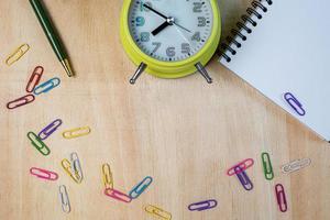 Notebook, pencil, clip, clock on wooden table photo