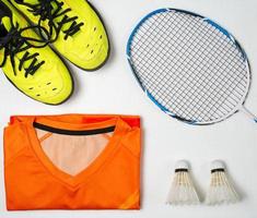 equipo de competición de bádminton, raqueta de bádminton, pelota de bádminton y zapatos sobre fondo de madera blanca foto