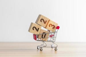 Happy new year with 2023 block in shopping trolley cart on table. E commerce, online shopping, finance, consumer economy and celebration concepts photo