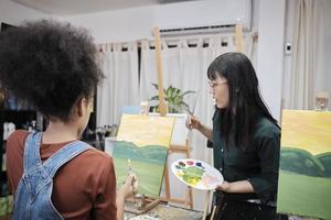 una maestra asiática enseña y demuestra a una estudiante sobre pintura acrílica en color sobre lienzo en el aula de arte, aprendiendo creativamente con habilidad en la educación de estudio de la escuela primaria. foto