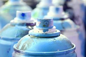 A lot of dirty and used aerosol cans of bright blue paint. Macro photograph with shallow depth of field. Selective focus on the spray nozzle photo