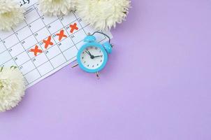 Blue alarm clock and white flowers on menstrual period calendar with red cross marks photo