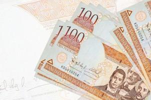 Los billetes de 100 pesos dominicanos se encuentran apilados sobre el fondo de un gran billete semitransparente. presentación abstracta de la moneda nacional foto