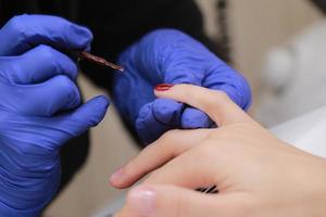 Master in protective gloves during a manicure at beauty salon. Master manicurist varnishes the marsala gel on the nails of a female client. The concept of beauty and health. photo