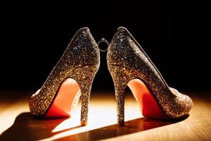 Golden ring with diamond between pair of bride shoes on dark background. selective focus photo