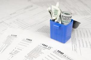 Many american tax blank forms and crumpled hundred dollar bill in trash bin photo