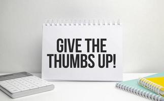 give the thumbs up words on paper notebook with office supplies photo