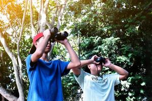 Southeast Asian boys are using binoculars to observe birds in tropical forest, idea for learning creatures and wildlife animals outside the classroom. photo