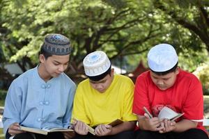 Group of muslim boys sit together under the tree in the school park, they also read, learn, talk, suggest and consult learning problems to each other, soft and selective focus. photo