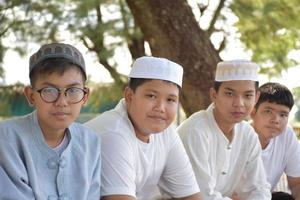 Young asian muslim boys sit in a row under the tree in the school park during their free times, soft and selective focus. photo