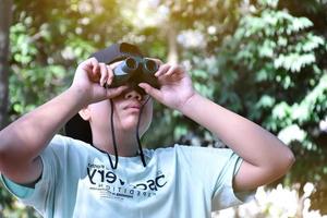 Southeast Asian boys are using binoculars to observe birds in tropical forest, idea for learning creatures and wildlife animals outside the classroom. photo