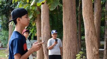 Three asian boys're reading birds details and going to use binoculars to watch birds on the trees during summer camp, idea for learning creatures and wildlife animals outside the classroom. photo