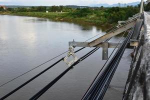 colgando y manteniendo el almacenamiento de cables de alta tensión y cables de fibra óptica en el costado de puentes fluviales de hormigón en las áreas remotas del sudeste asiático, enfoque suave y selectivo. foto