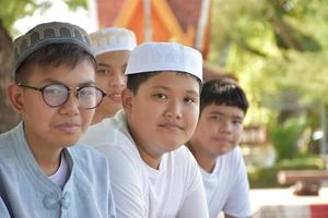 Young asian muslim boys sit in a row under the tree in the school park during their free times, soft and selective focus. photo