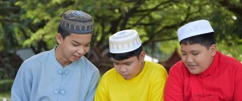 Group of muslim boys sit together under the tree in the school park, they also read, learn, talk, suggest and consult learning problems to each other, soft and selective focus. photo