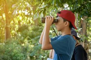 Southeast Asian boys are using binoculars to observe birds in tropical forest, idea for learning creatures and wildlife animals outside the classroom. photo