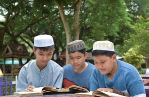 jóvenes asiáticos musulmanes o islámicos sentados juntos en el parque escolar para leer, aprender, hacer y consultar la tarea y esperando aprender temas religiosos en la escuela, enfoque suave y selectivo. foto