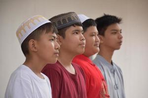 jóvenes asiáticos musulmanes o islámicos parados en fila frente a la pared blanca de la mezquita, enfoque suave y selectivo. foto