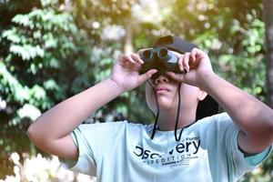 Southeast Asian boys are using binoculars to observe birds in tropical forest, idea for learning creatures and wildlife animals outside the classroom. photo