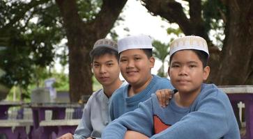 jóvenes asiáticos musulmanes o islámicos sentados juntos en el parque escolar para leer, aprender, hacer y consultar la tarea y esperando aprender temas religiosos en la escuela, enfoque suave y selectivo. foto