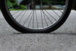 Rear wheel of bike which is flat and parked on the pavement beside the road. photo