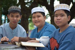 jóvenes asiáticos musulmanes o islámicos sentados juntos en el parque escolar para leer, aprender, hacer y consultar la tarea y esperando aprender temas religiosos en la escuela, enfoque suave y selectivo. foto