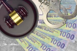 1000 Indonesian rupiah bills and judge hammer with police handcuffs on court desk. Concept of judicial trial or bribery. Tax avoidance photo