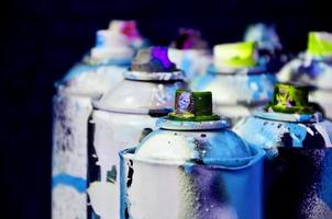 Still life with a large number of used colorful spray cans of aerosol paint lying on the treated wooden surface in the artist's graffiti workshop. Dirty and stained cans for spray art photo