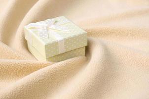 A small gift box in orange with a small bow lies on a blanket of soft and furry light orange fleece fabric with a lot of relief folds. Packing for a gift to your lovely girlfriend photo