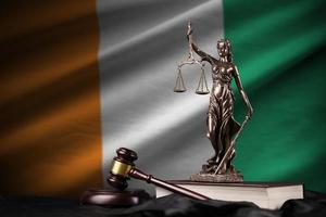 Ivory Coast flag with statue of lady justice, constitution and judge hammer on black drapery. Concept of judgement and guilt photo