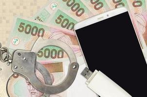 5000 Indonesian rupiah bills and smartphone with police handcuffs. Concept of hackers phishing attacks, illegal scam or malware soft distribution photo