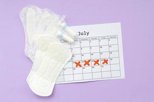 Menstrual pads and tampons on menstruation period calendar flat lay on lilac background photo