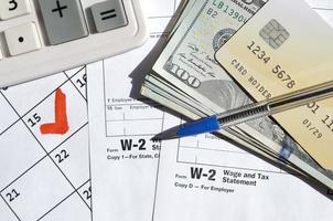 W-2 Wage and Tax statement blank with credit card on dollar bills, calculator and pen on calendar page with marked 15th April photo