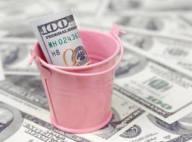 A bundle of US dollars in a metal pink bucket on a set of dollar bills photo