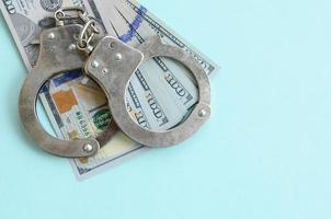 Silver police handcuffs and hundred dollar bills lies on light blue background photo