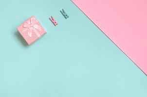 una pequeña caja de regalo rosa y dos clavijas se encuentran en el fondo de textura de papel de colores azul pastel y rosa de moda en un concepto mínimo foto