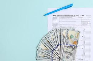 1041 tax form lies near hundred dollar bills and blue pen on a light blue background. US Income tax return for estates and trusts photo