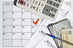 W-2 Wage and Tax statement blank with credit card on dollar bills, calculator and pen on calendar page with marked 15th April photo