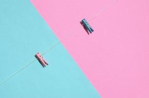 Two colored wooden pegs and small rope lie on texture background of fashion pastel blue and pink colors paper in minimal concept photo