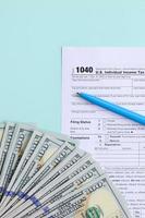 El formulario de impuestos 1040 se encuentra cerca de los billetes de cien dólares y el bolígrafo azul sobre un fondo azul claro. Declaración de impuestos sobre la renta de las personas físicas de EE. UU. foto
