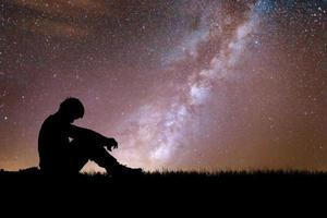 Loneliness, despair and regret concept. Lonely man in the meadow against the backdrop of stars and the Milky Way.