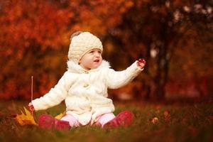 beautiful little baby girl sitting with a big leaf at autumn park photo
