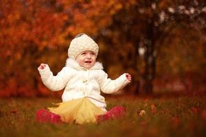 beautiful little baby girl sitting with a big leaf at autumn park photo