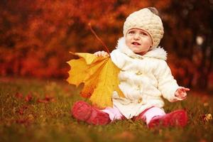hermosa niñita sentada con una hoja grande en el parque de otoño foto