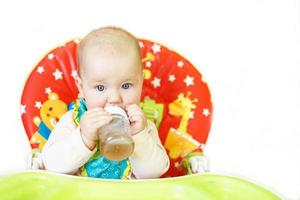 baby drinking from bottle sitting in high chair on a white background photo