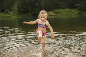 Little cute girl have fun playing with a spray of water in the river at summer. copy space photo