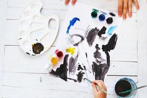 view from above. child draws a brush and paints top view. Flat lay art tools for painting.Artwork workplace photo