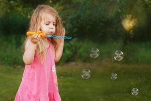 Cute little girl is blowing soap bubbles photo