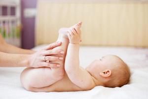 Mom does gymnastics for a child. Mother massaging baby in bed at home. photo