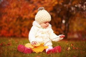 beautiful little baby girl sitting with a big leaf at autumn park photo